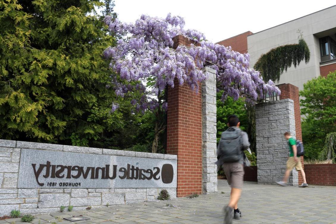 Seattle University sign at south entrance with people walking on sidewalk